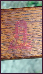 Gustav Stickley's red decal mark featuring the words "Als Ik Kan" within a joiners compass.